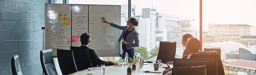 Policy analyst in a meeting pointing to a whiteboard