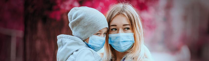 Mom holding daugther while both are wearing masks in public